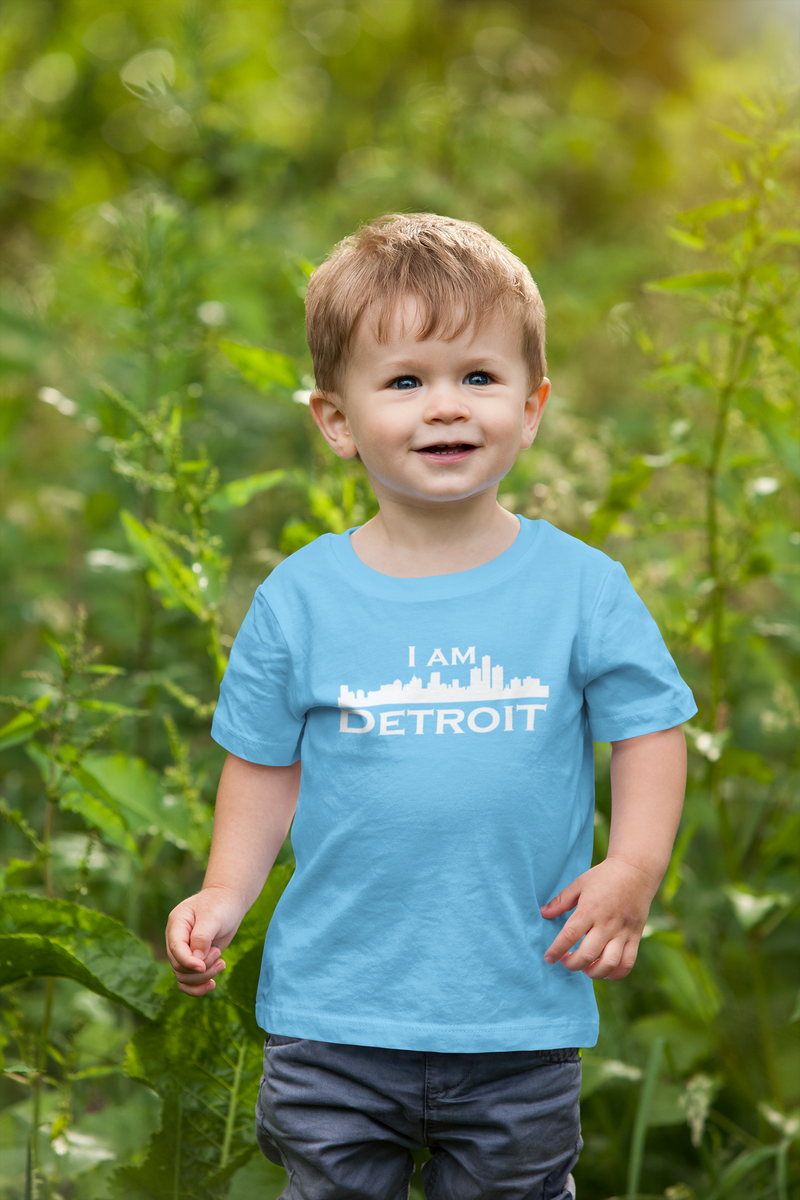Cute smiling little boy in a field wearing a light blue t-shirt with a white I Am Detroit logo printed across the chest