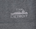 Close up of I Am Detroit logo near hem at bottom on the back of a gray hooded sweatshirt 