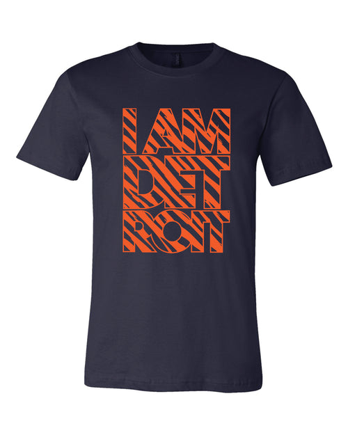 Orange tiger stripes fill large block lettering that reads I Am Detroit on the front of a navy blue T-shirt